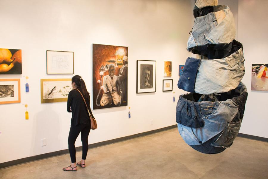 Jose Solis sculpture entitled Bound to Denim suspends from the ceiling as attendees of the Annual Student Exhibition exit on Friday, April 25, in the Atkinson Gallery at City College. Solis sculpture is comprised of denim, buttons and zippers with an asking price of $10,000.