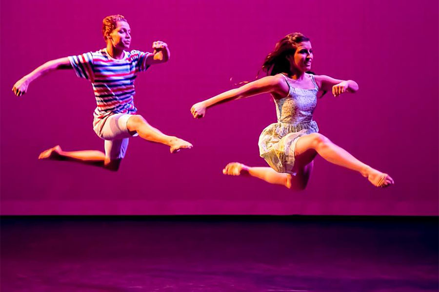 Two dancers leap across a stage.