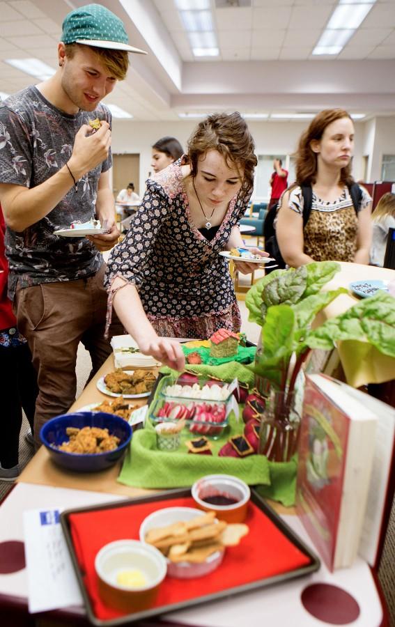 Graphic design major Brendan Sugrue, 20, stands with environmental studies student Bella Strid, 22 while she goes for a radish on one of the more healthier options at the 6th Edible Book Festival on Wednesday afternoon, March 23, in City Colleges Luria Library.
