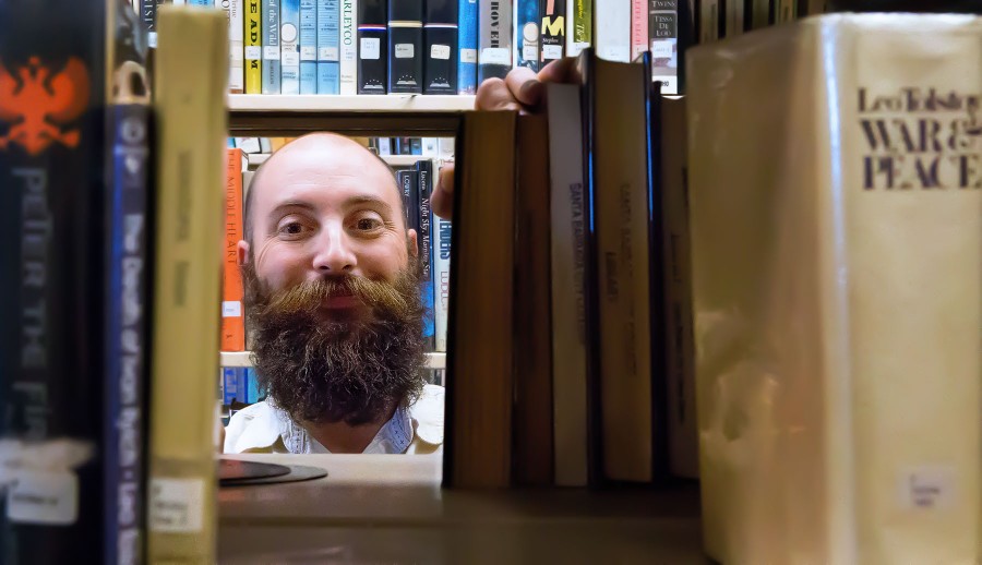 Library Assistant Loren Mindell stands with the book collection written by one of his favorite authors, Leo Tolstoy, on Thursday afternoon, April 7, at the Luria Library in Santa Barbara. Mindell is one of the newest staff members at the school’s library.