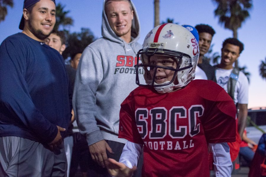 (From left) Defensive linemen for the City College football team Timothy Nunez and Tristan Harris high five 9-year-old Beckett Smalldon, dressed as a City College football player, during the Trunk or Treat event Friday, Oct. 27, held at the parking lot adjacent to La Playa Stadium.