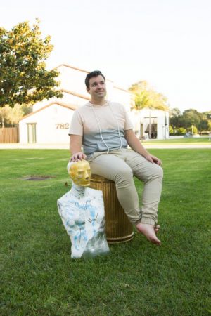 City College art student Bryan Austin Gillison, sitting on a golden trash can he uses as a pedestal, outside his apartment Friday, Oct. 13, in Goleta, Calif. “The golden trash can is a good metaphor for what I do because it’s like gilded trash,” said Gillison 