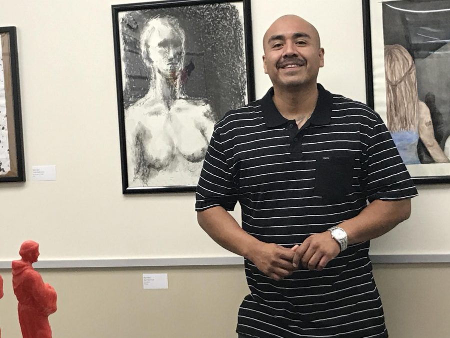 Commencement speaker Alberto Lule stands in front of his pop-up art show, “The Monster in my Closet” located in the Equity Center May 11, 2018. Lule was previously incarcerated and said he found a passion for art in prison, which lead him to obtaining three art degrees.