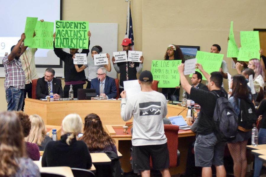 Student protesters surround Board of Trustees members Thursday while holding signs in silent protest of the return of Vice President of Business Services Lyndsay Maas to the college. Maas has been on unpaid leave since November after using the un-abbreviated version of the n-word at an equity meeting.