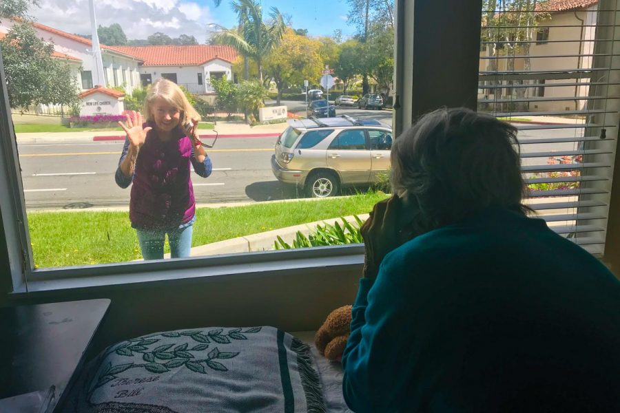 Mary Orr waves during a visit with her friend Eileen Carlson through a window of the Villa Alamar Retirement Community. Carlson is a resident at Villa Alamar and is allowed to communicate with friends and family on the phone through the window under house policy. Photo courtesy of Luciana Mitzkun Weston.