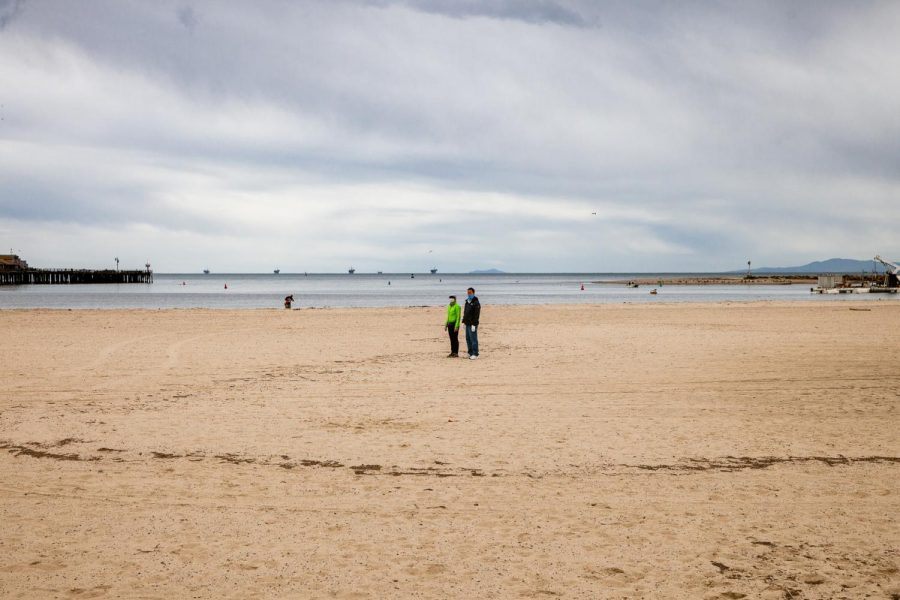 Beach goers stand gazing out over an empty West Beach near Stearns Wharf, one of the few citizens out due to statewide shelter-in-place orders brought on by the novel coronavirus.