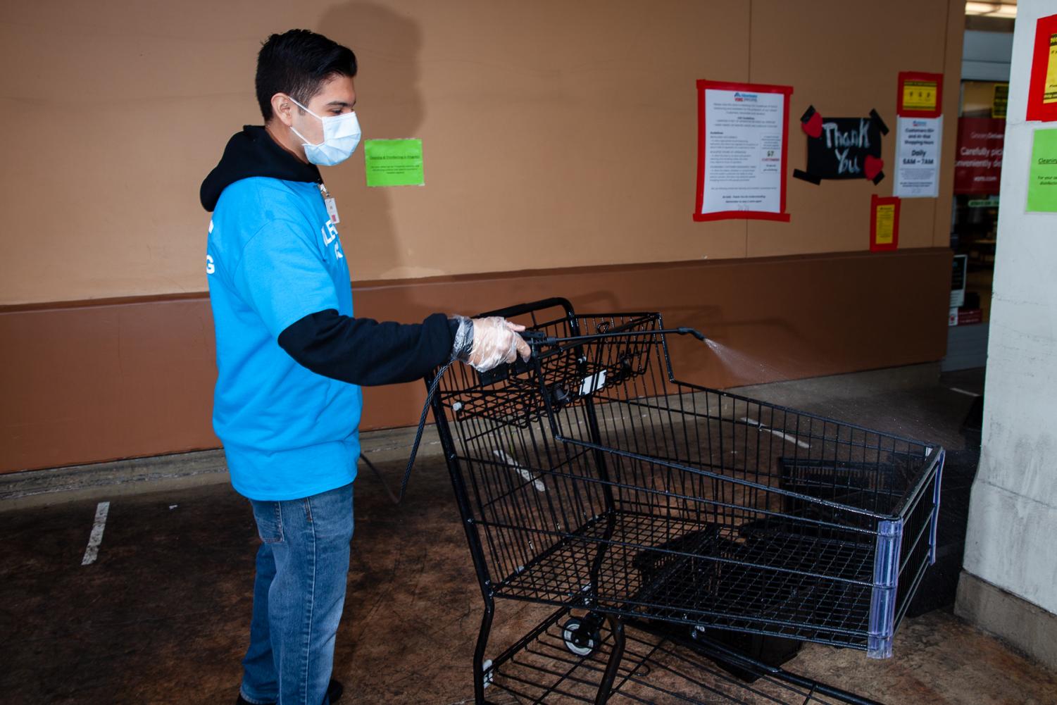 Dario Alonso sprays a disinfectant solution on shopping carts at Vons Supermarket on The Mesa on Thursday April 9, in Santa Barbara, Calif. Alonso started working two weeks ago to help his mother pay rent after she lost her job due to coronavirus precautions. 