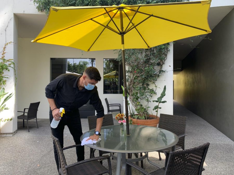 Server Luka Djuranovic wipes down a table during the sanitizing routine that is done after the customers are done eating on Sept. 17, 2020 at Crocodile Restaurant & Bar in Santa Barbara, Calif. Djuranovic regularly reminisces on when customers were able to come in and enjoy the bar and seats indoors during these routines.