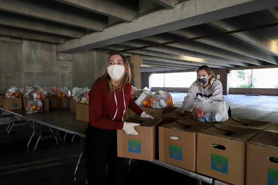 Megan Mcgill (left), and Astrid Bladh grab and organize the boxes of pre-packaged fresh produce and non-perishables that are placed in the back of students cars at the food distribution event in the West Campus Lot 5-1 on Wednesday Feb. 10, 2021 in Santa Barbara, Calif. Mcgill has been volunteering with the food distribution services for a couple weeks and said that “it’s good to know that we are helping people.”