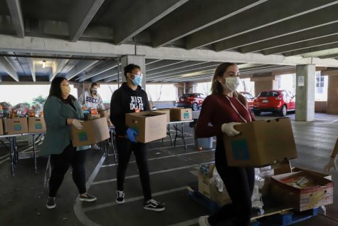 From left Aranzazu Magallanes, Jirehandre Bitangila, and Megan Mcgill carry boxes of pre-packaged fresh produce and non-perishables to a students car at the food distribution event in the West Campus Lot 5-1 on Wednesday Feb. 10, 2021 in Santa Barbara, Calif. The boxes have fresh produce such as celery, apples and milk along with items like bread and pasta as well.