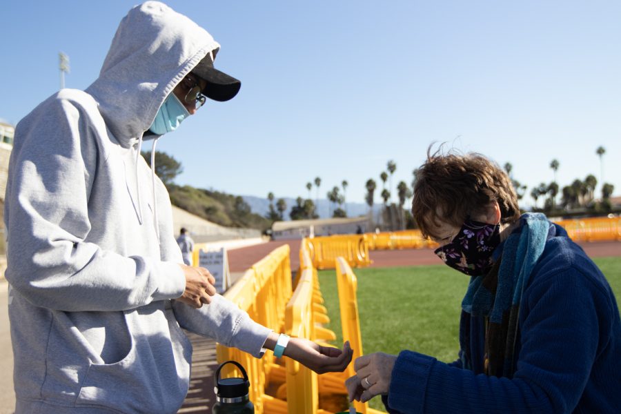 A physical education student holds out his arm for City College physical instructor E. Bonnie Lewis to apply a wristband for campus entry on Tuesday, Nov. 23 at City College's La Playa Stadium in Santa Barbara, Calif. Besides checking in students four days a week, Lewis primarily works as a fitness stretching instructor.