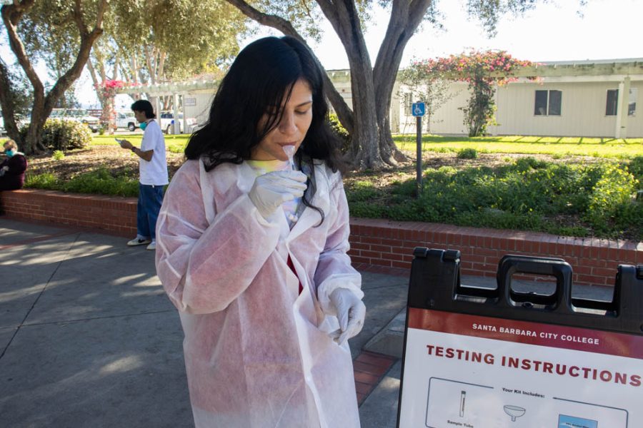 Nurse Ariana Romo demonstrates how to properly take a COVID-19 spit test on Feb. 7 at City College in Santa Barbara, Calif. In order to enter a building on City Colleges campus, individuals need to upload their vaccination status or proof of exemption, submit a negative COVID-19 test once a week and wear an N95 or KN95 mask.