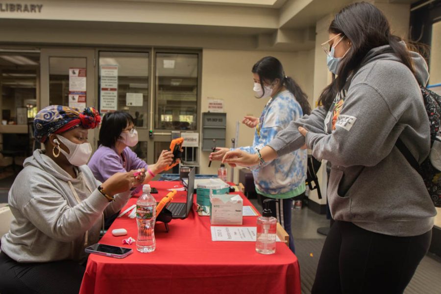 From left, student worker and ASG President Allegra Kabukapua Kalombo prepares a wristband while her coworker signs a student in by scanning their phone on Wednesday, Feb. 23 at City Colleges Luria Library in Santa Barbara, Calif. Anyone intending on entering a building on campus must provide proof of COVID-19 vaccination and a negative test or an approved exemption for the week of Feb. 22.