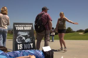 Elizabeth Saffer discusses with an anti-abortion protester on SBCC's Great Meadow on Wednesday, April 19 in Santa Barbara, Calif. The sign beside Saffer displays an ultrasound reading "The body inside your body is not your body."
