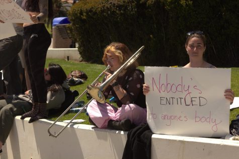 Bella Duncan (left) plays the trombone over the anti-abortion presentation beside a student holding a sign reading "Nobody's entitled to anyone's body" outside of the Luria Library on March 15 in Santa Barbara, Calif. Duncan passed by in between her music classes, and provided a soundtrack during the protest.