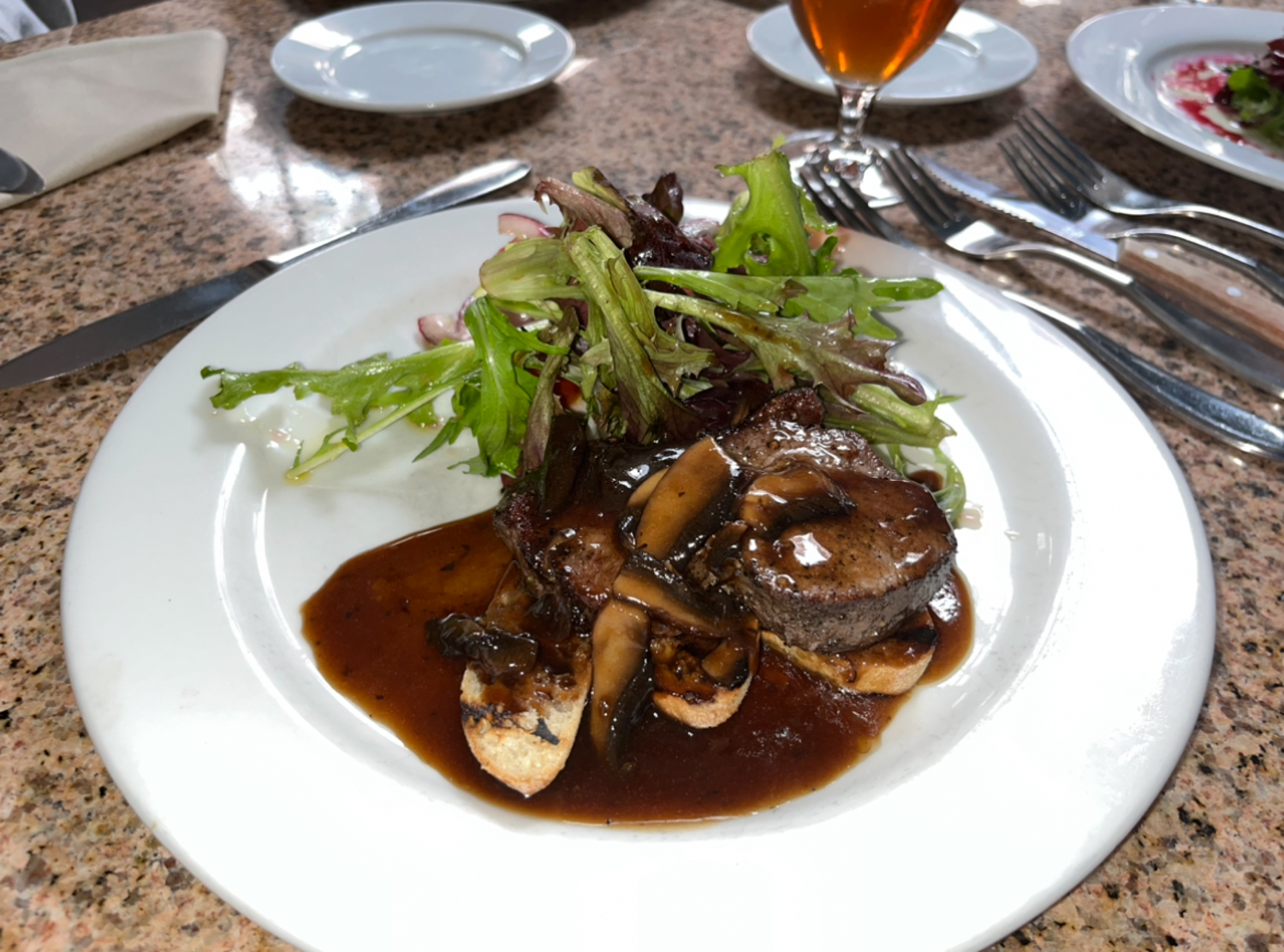 A piece of steak accompanied with sides sits on a table on Tuesday, May 9 at Petit Valentein located in Santa Barbara, Calif. The steak was served with a mushroom crostini and a side salad consisting of lettuce, onion, fresh tomato and a drizzle of olive oil.