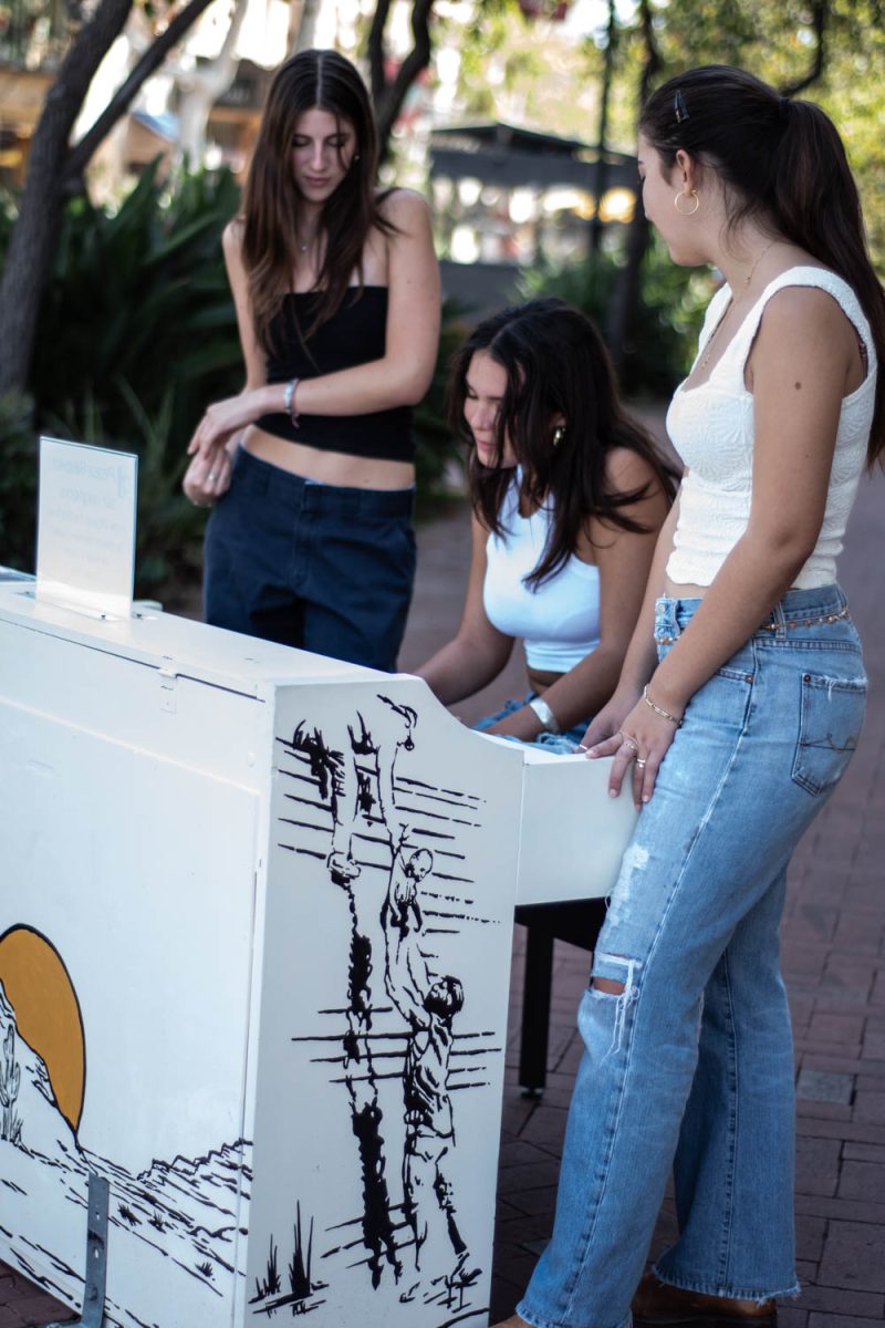 Friends Desray **QC** Castelo (left) and Emma Thom (right) encourage Jasmyn Dennis (center) as she tries to remember the songs she learned from her childhood piano lessons on Oct. 12 on the corner of Victoria and State streets in Santa Barbara, Calif. "It's the biggest thing that irks me about myself: I can't remember," Dennis says.