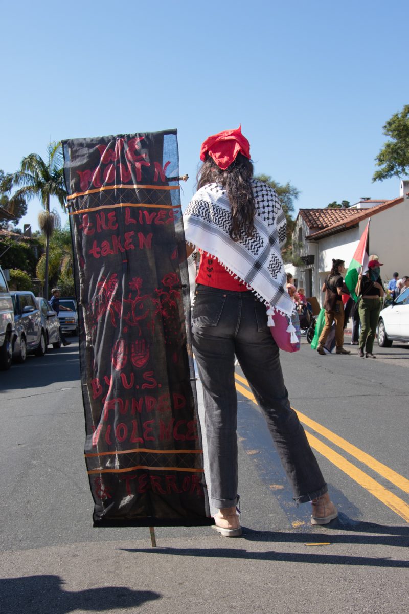 A protester blocks the road on De La Guerra street so that Jewish Voice for Peace members and supporters can cross the street and continue in chants outside of Congressman Carbajal's office on Oct. 24 in Santa Barbara, Calif. Her sign reads "we mourn the lives taken by U.S. funded violence and terror."