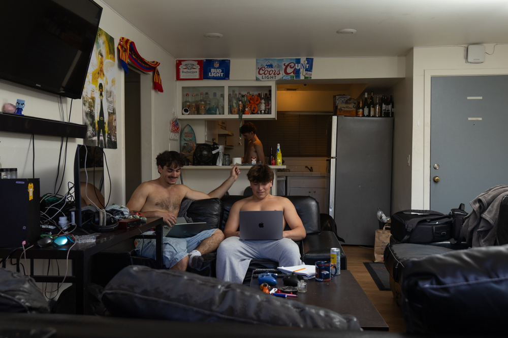 In a two-bedroom apartment shared by five students, Charlie Platt prepares food while his roommate Nico Kemp and their friend Cooper Call catch up on schoolwork April 19 at the Beach City complex in Santa Barbara, Calif. Student apartments often double as study spots and social hubs.