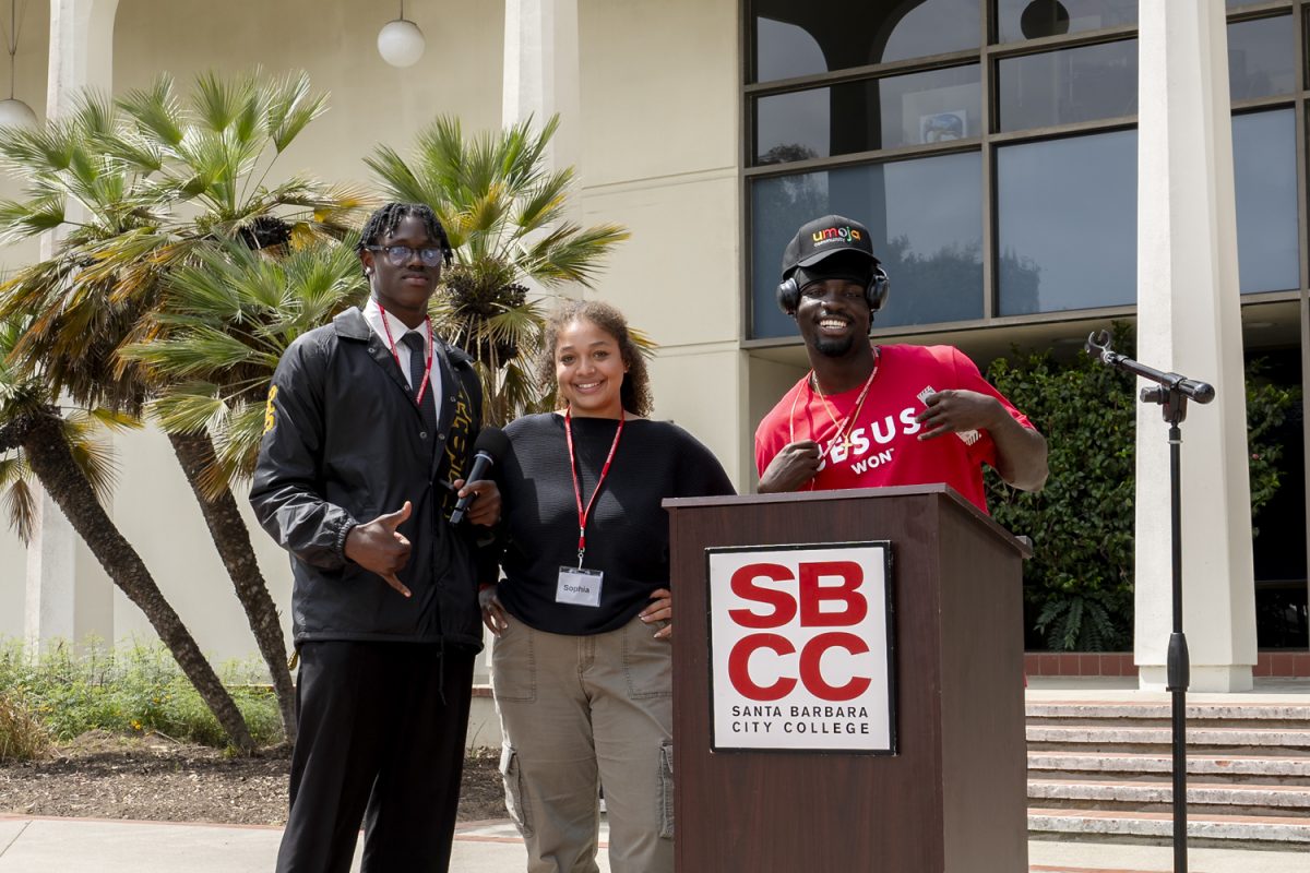 From left, Ewomazino Asidi, Sophia La Riviere, and Thomas Ngure pose for a photo in front of the City College logo during the first-ever Umoja Day on April 25 in Santa Barbara, Calif. The three stand together at the podium, marking a memorable moment at the event.
